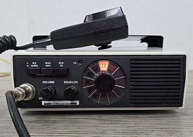 VHF-FM unit with round channel selector, 2 other knobs, 3 push buttons, speaker and a microphone laying on top